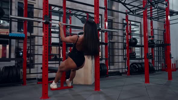 a Muscular Brunette with Long Hair and in a Black Swimsuit Performs Horizontal Pullups in the Gym