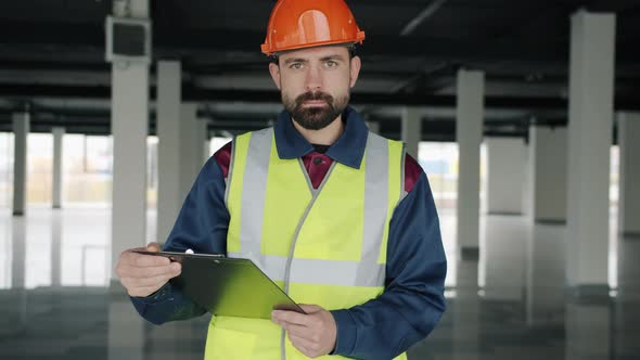 Portrait of Construction Specialist Standing in Workplace with Papers and Looking at Camera