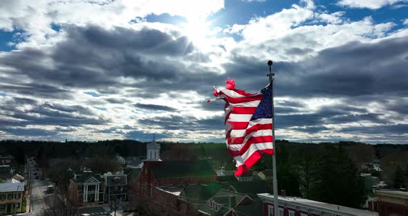 Tired old American flag. Tattered USA red white and blue waves on sunny windy daytime. Bright sunlig