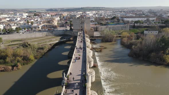 Tourist walking on Cordoba Roman bridge on sunny day, Spain. Aerial flyback