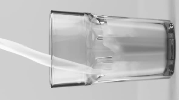 Vertical Video Milk Pouring Into Faceted Glass Close Up Isolated on Light Grey Background