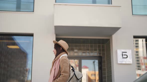 A Girl in a Beige Fur Coat Walks Along the Building