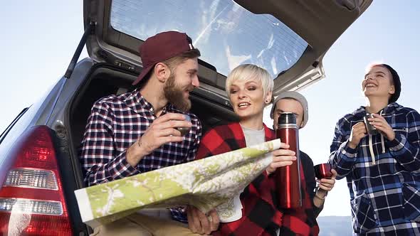 Tourist Drinking Hot Coffee or Tea Looks at the Roadmap while Leaning on the Car