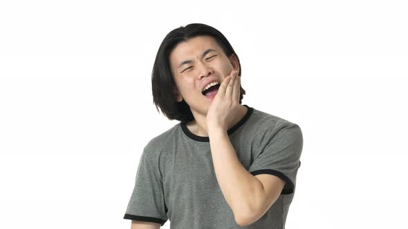 Portrait of Frowing Chinese Man in Casual Gray Tshirt Suffering From Toothache and Touching Jawbone