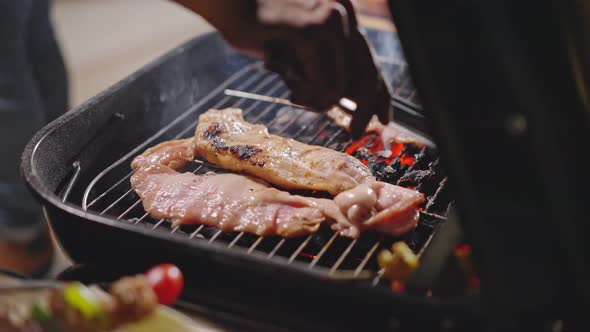 Close up of barbeque grilling meat burning fire with smoke on bbq grid at dark night in camp.