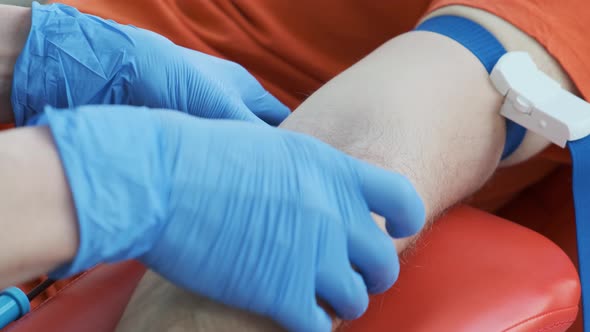 Nurse Inserts a Needle Into a Vein. Medical Worker with Protective Gloves Does a Blood Sampling for