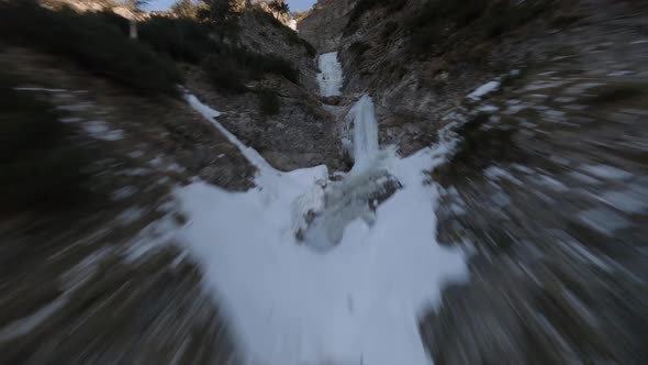 fpv drone flying up on a frozen waterfall at an austrian mountain in spring at sunset