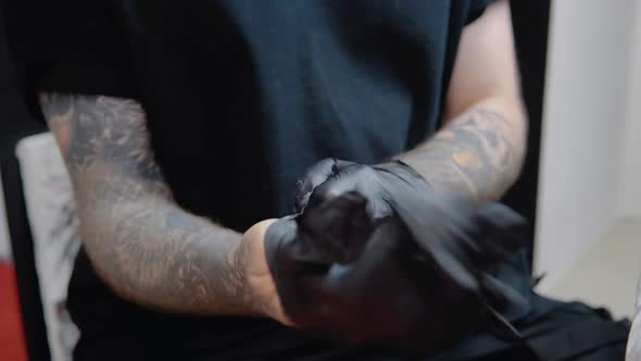 Tattoo Master with Tattooed Hands Wears Sterile Gloves and Disinfects His Hands Before Working with
