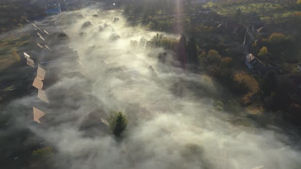 Flying Above a Remote Village Covered in Morning Haze and Mist in Early Morning Lights alt