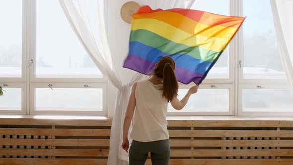 Female Holding LGBT Gay Flag in Hands and Waving on Sunset in Sunny Rays