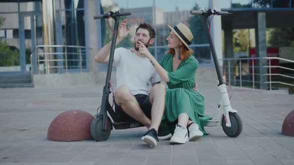 Young Lovely Couple Sitting and Having Fun with Electric Scooters