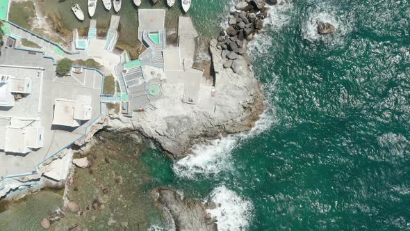 Aerial Overhead Top Down View of Greek Fishing Village with Waves Crashing Into Rocks on Milos