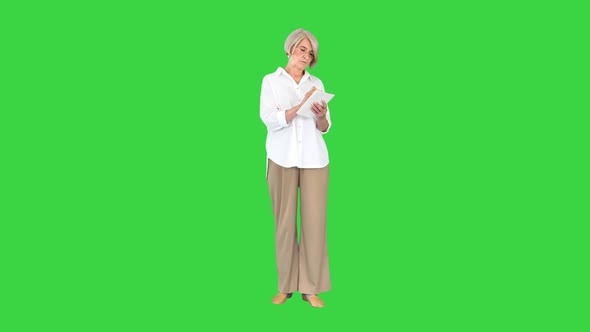 Senior Woman Making Notes in Notepad on a Green Screen Chroma Key