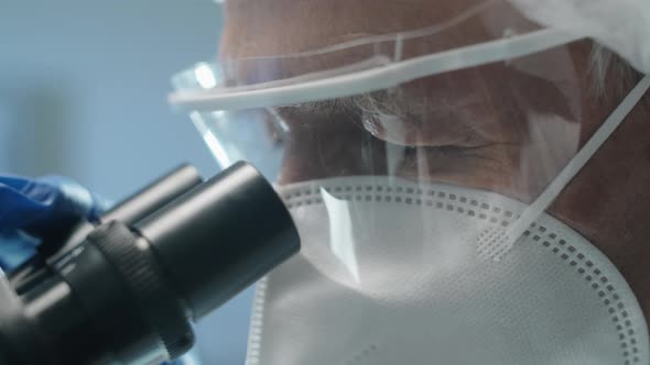 Senior Scientist in Protective Uniform Looking through Microscope