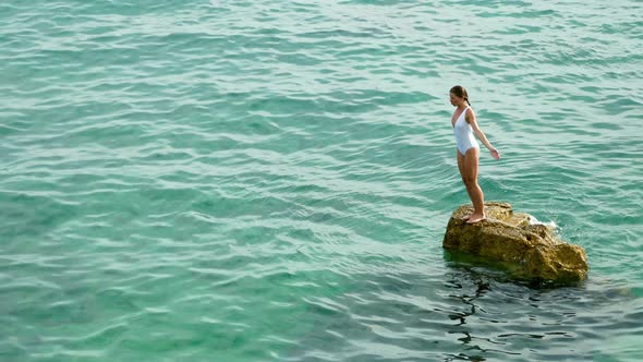 Woman jumping from a stone to the sea