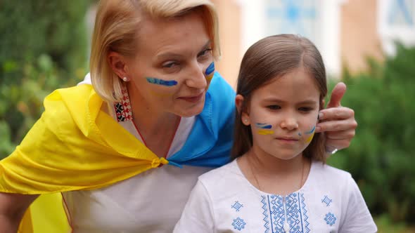 Loving Ukrainian Mother Drawing on Face of Pretty Daughter with National Flag Colors and Looking at