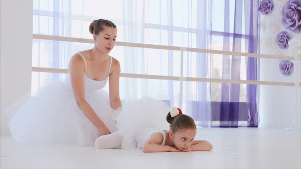 Little Ballerina in White Tutu is Stretching in Frog Pose with Ballet Teacher