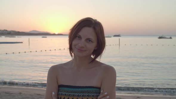 Portrait of 30s Woman in Dress Standing on the Beach at Sunrise Over the Sea