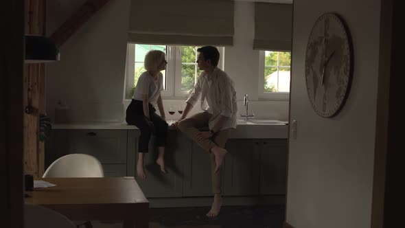 Young Couple in Love Sitting in the Kitchen Flirting and Drinking Wine