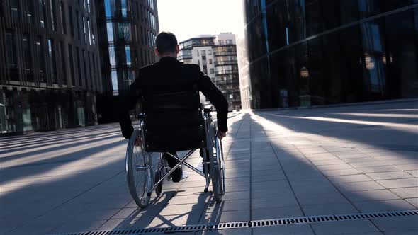 Back View of a Invalid Businessman in Wheelchair Moves in Business District.