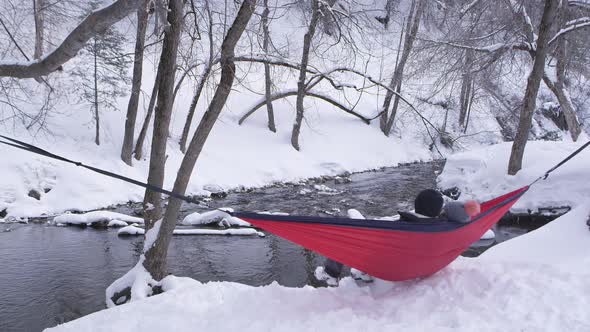 Couple sitting in hammock tied up outside in the snow by river