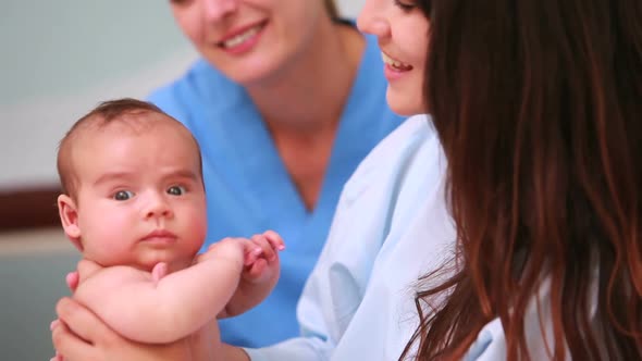 Woman holding a baby next to a nurse