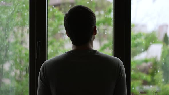 Silhouette of a Man Looks Outside the Window at the Rain