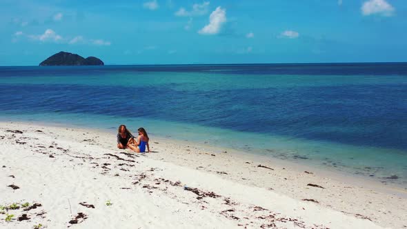 Ladies together happy and smiling on relaxing coastline beach vacation by transparent ocean and whit