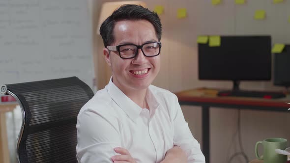 Close Up Of Asian Man Crossing Arms And Smiling To Camera While Working With Documents At The Office