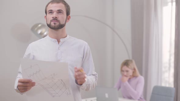 Portrait of Confident Caucasian Man Looking Around Room and Taking Notes in His Drafts