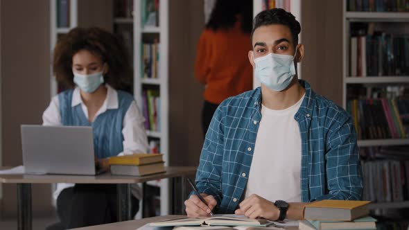 Students Sitting in Library Studying Young Happy Guy in Medical Mask Sits at Desk Preparing for Exam