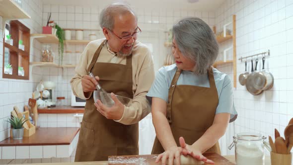 Asian senior older couple, Husband stirring eggs, wife threshing the flour, helping each other cook.