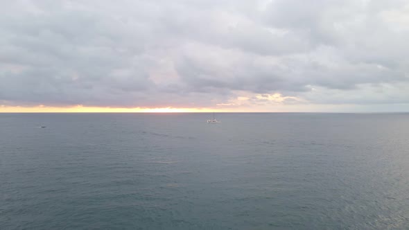 backwards drone flight over the ocean away from a nice orange sunset and a ship