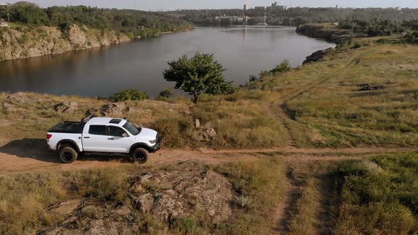 A white car rides along a winding road along the river off-road outside the city