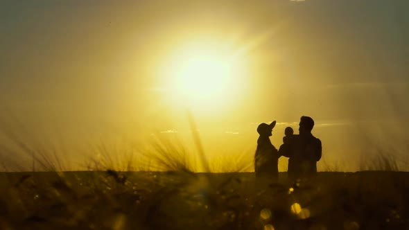 Silhouettes of Parents and Baby in Field at Sunset