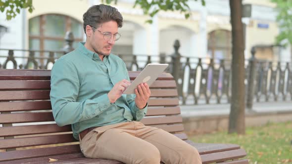 Man using Tablet while Sitting on Park Bench