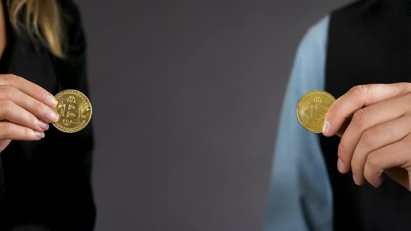 Detail of male and female hand holding two gold bitcoin coins,close up.