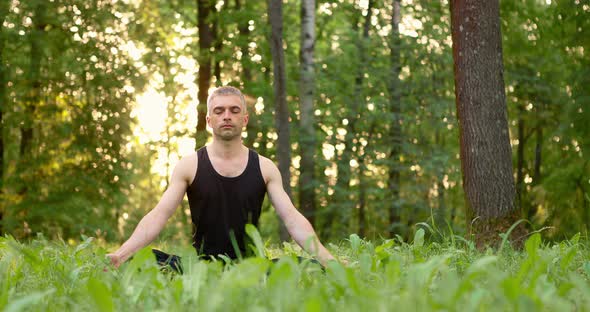 Young Man Sitting on Lawn Doing Meditation in City Park