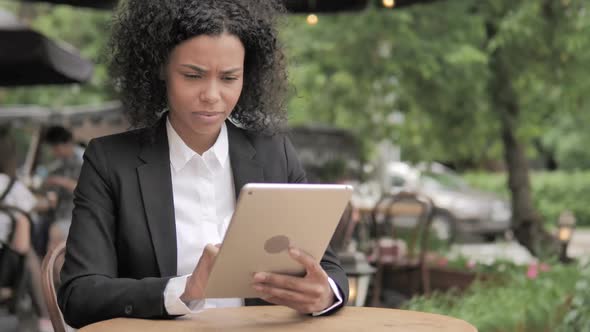 Shocked African Woman Upset By Loss on Tablet Sitting in Outdoor Cafe