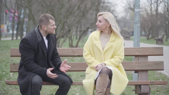 Angry Caucasian Man Scolding Beautiful Blond Woman As Sitting on Bench in Park. Unhappy Family