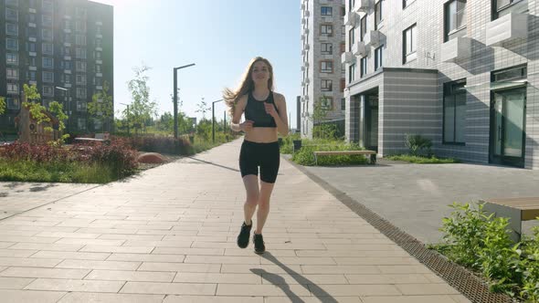 Athletic Brunette Woman in Black Tight Sportswear Runs Along Alley of Residential Complex in Morning