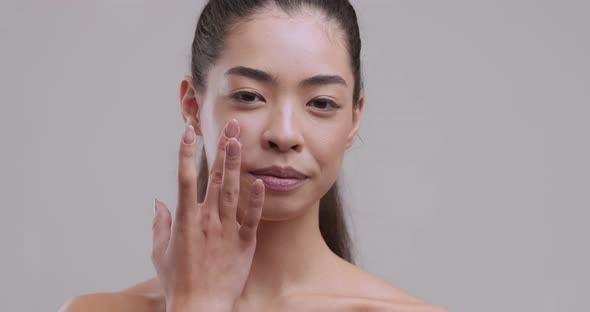 Portrait of Young Asian Woman Applying Cream Smear on Cheek and Smiling To Camera