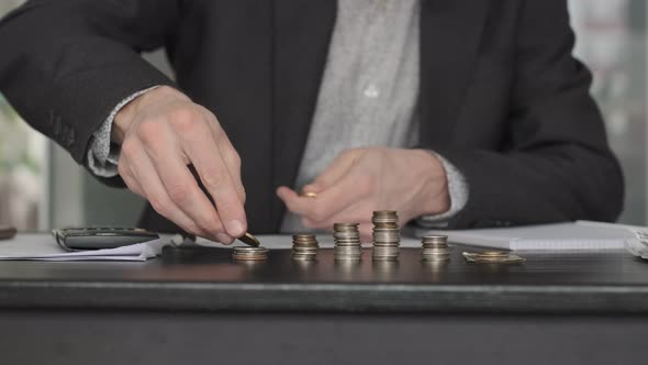 Male Hand Stacking Coins and Counting on Table