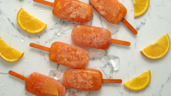 Homemade Frozen Popsicles Made with Oragnic Fresh Oranges Placed with Ice Cubes on Marble Table