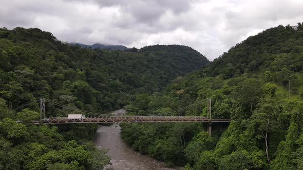 Drone slowly approaching a run-down steel bridge surrounded by thick rainforest in the middle of now