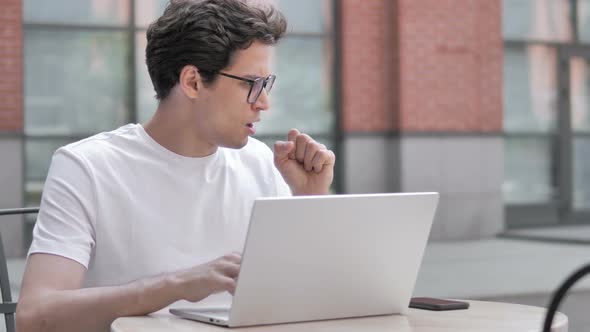 Sick Young Man Coughing while Working on Laptop Outdoor