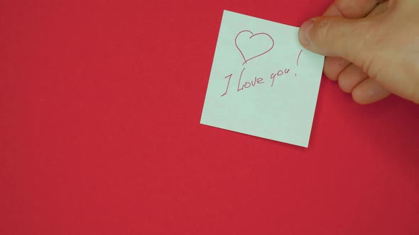 Male Hand is Pasting Sticker with the Words I Love you is Written in Pen and Drawn with a Heart for