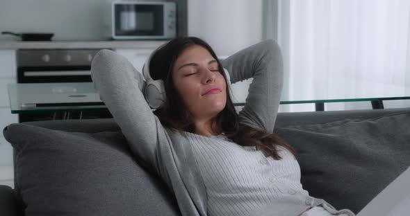 Serene Millennial Girl Listening to Musicin Headphones Resting on Couch Taking Deep Breath of Fresh