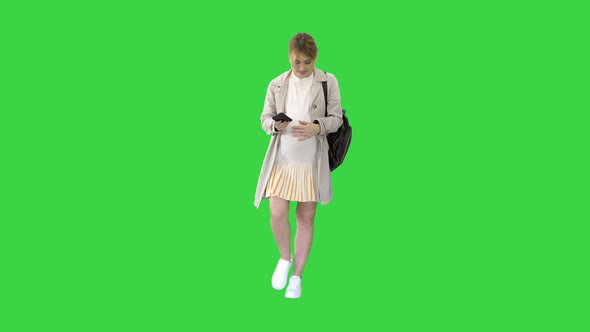 Pregnant Girl with Phone in Hand Walking on a Green Screen, Chroma Key.