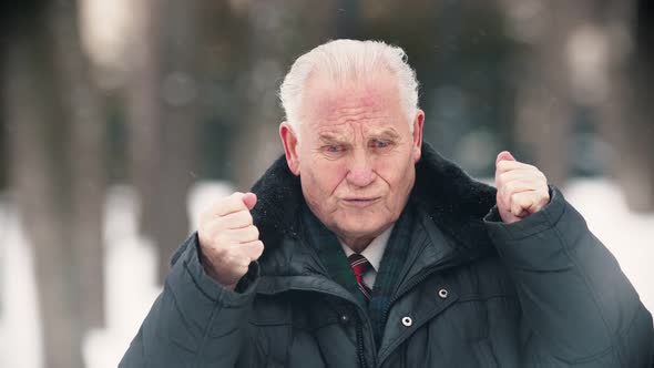 An Old Man Standing Outdoors While Snowfall - Putting His Hands Up